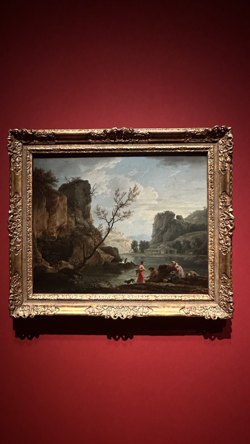 A landscape painting in a gilt frame on a red gallery wall